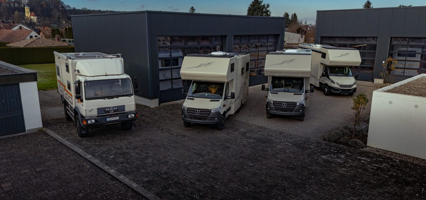 Verschiedene Wohnmobile stehen vor modernen Garagen in einer ruhigen Umgebung.